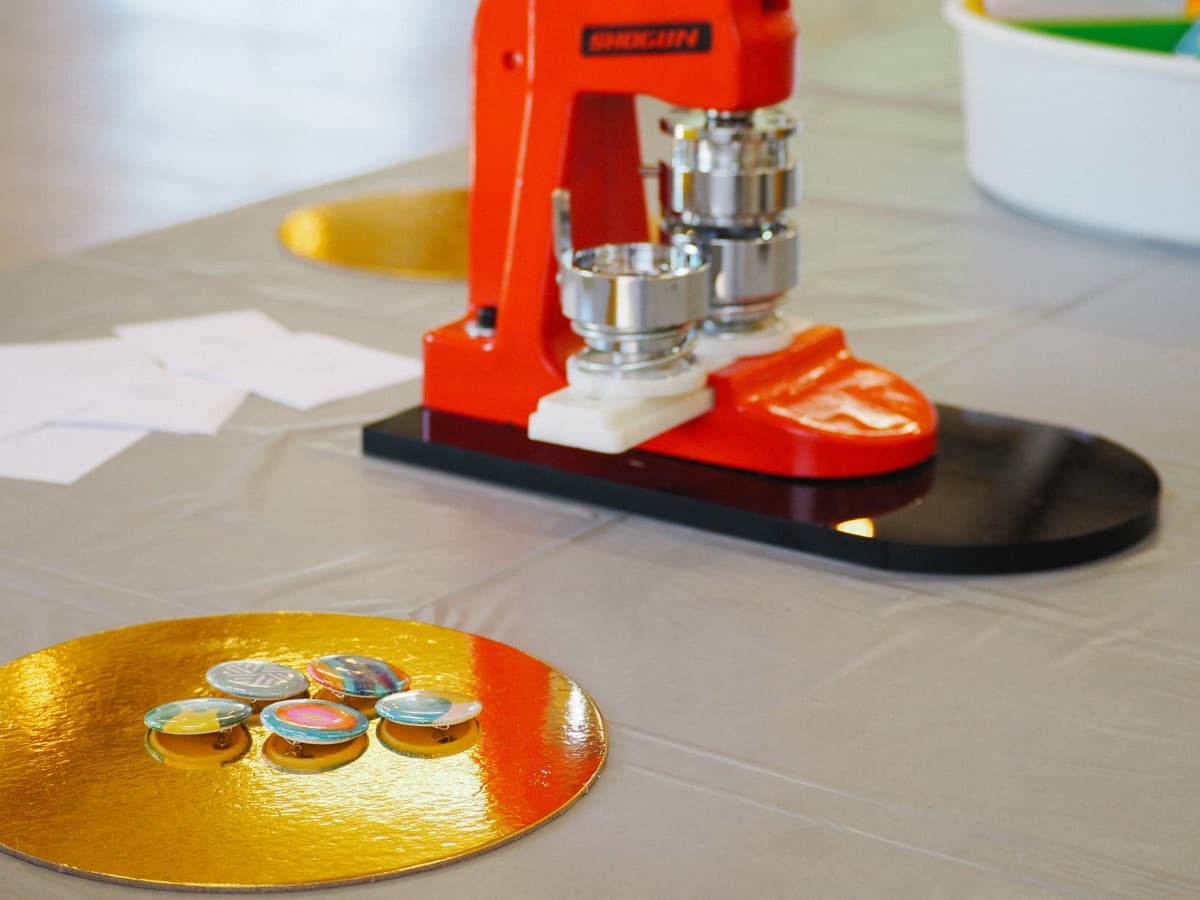 A button badge press machine on a table with freshly made colourful badges on a gold disc.