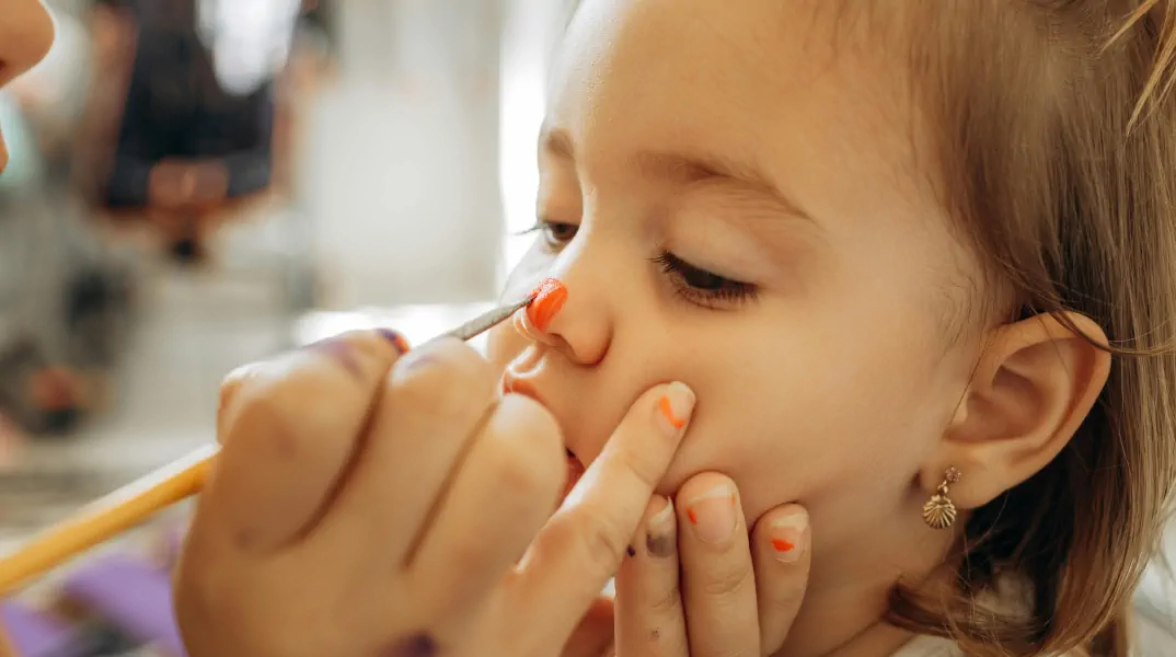 Child's face being painted with vibrant colours, highlighting intricate details on the nose.