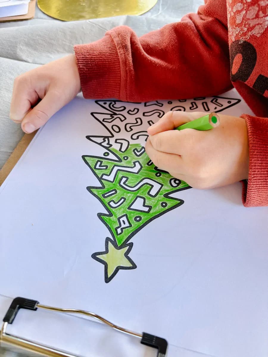 Child's hands colouring a Christmas tree illustration with a green marker at an Event Sitters craft session