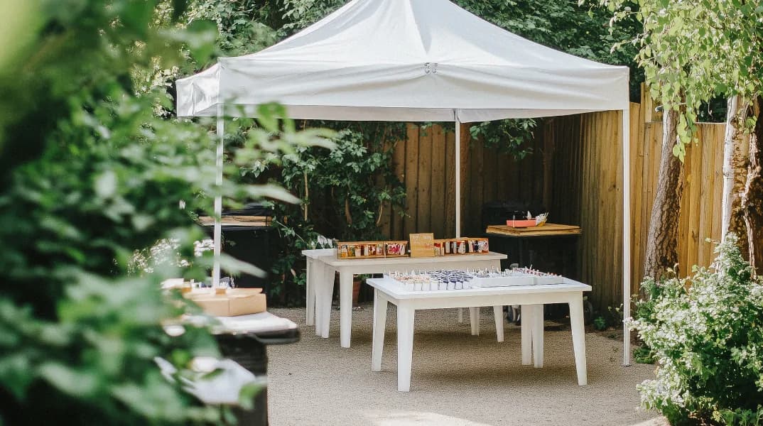 Outdoor craft setup under a white canopy, featuring tables with art supplies in a lush garden environment.