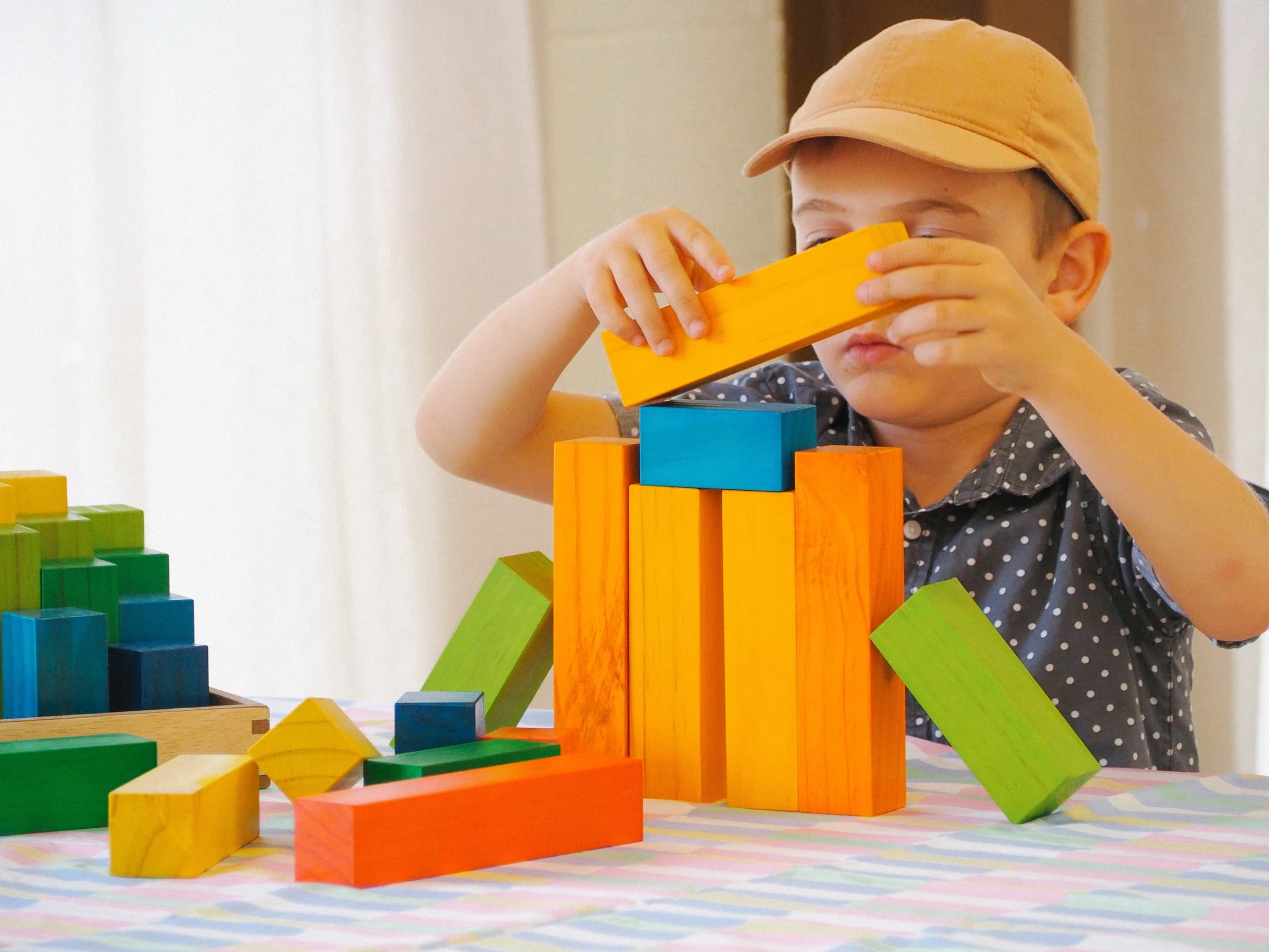 Young boy in a cap concentrating on building a tower with colourful wooden blocks